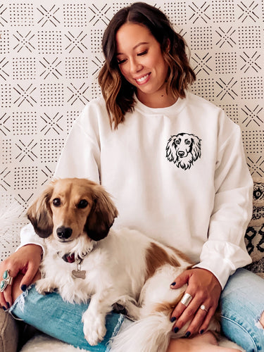White long haired Dachshund sweatshirt modeled by a woman sitting on a couch with a long haired dachshund in her lap.